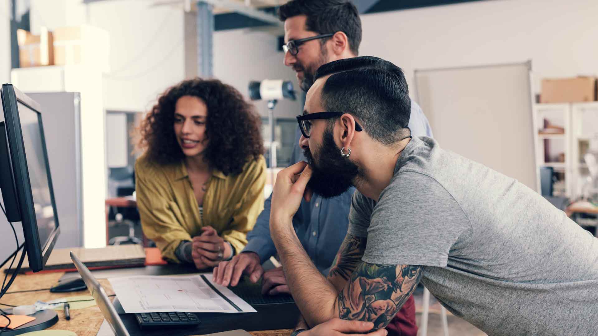 Team of three working together to solve a problem on a computer in an office.