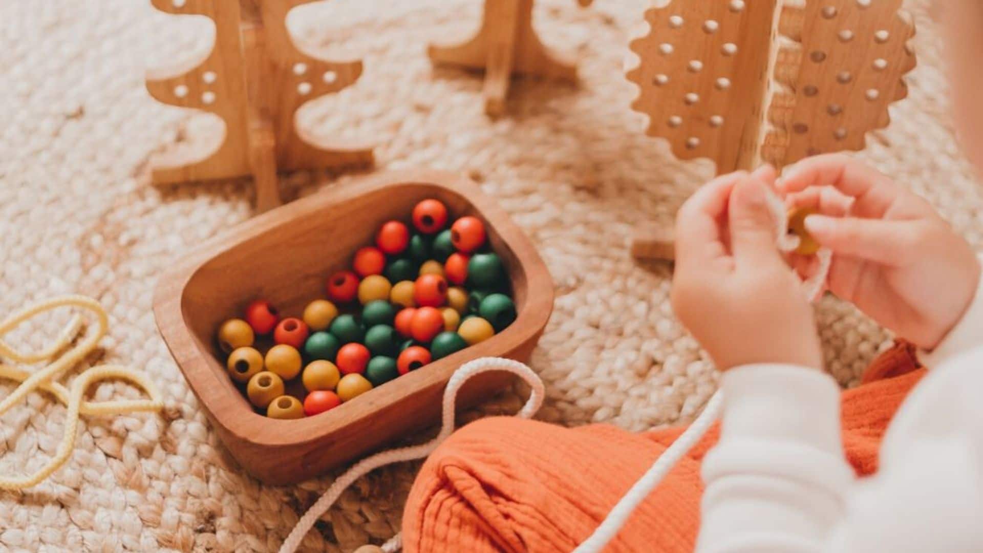 A child threads a rope through a bead with a wooden bowl of coloured wooden beads in the background