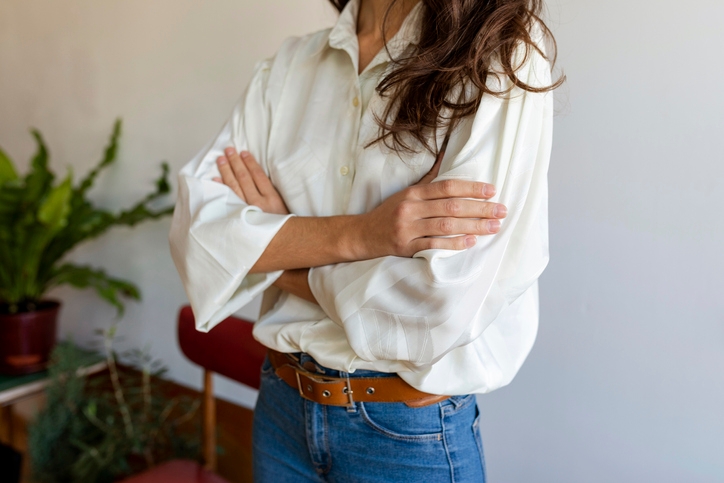 Woman stands arms crossed in a white blouse and denim jeans 