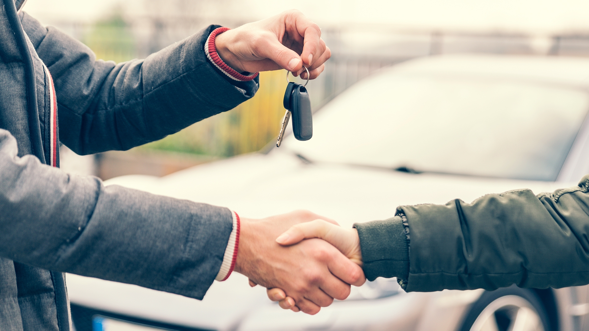 Two people shaking hands and passing car keys in front of vehicle