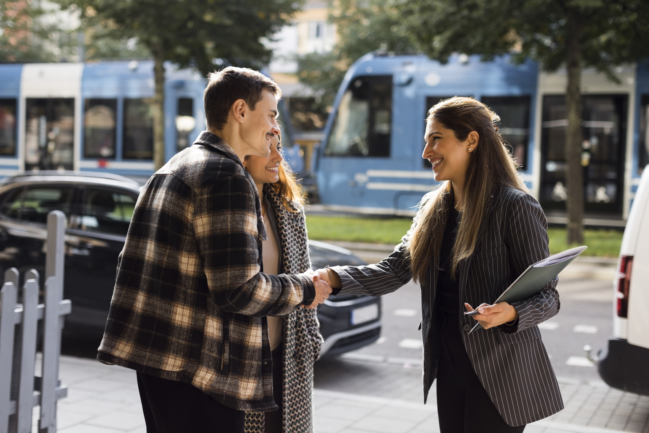 Female real estate agent holding a folder and shaking hands with prospective buyers on the street