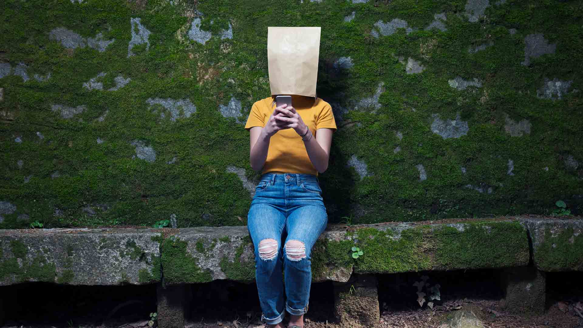 Embarassed person sitting with a paper bag over their head to hide their identity.