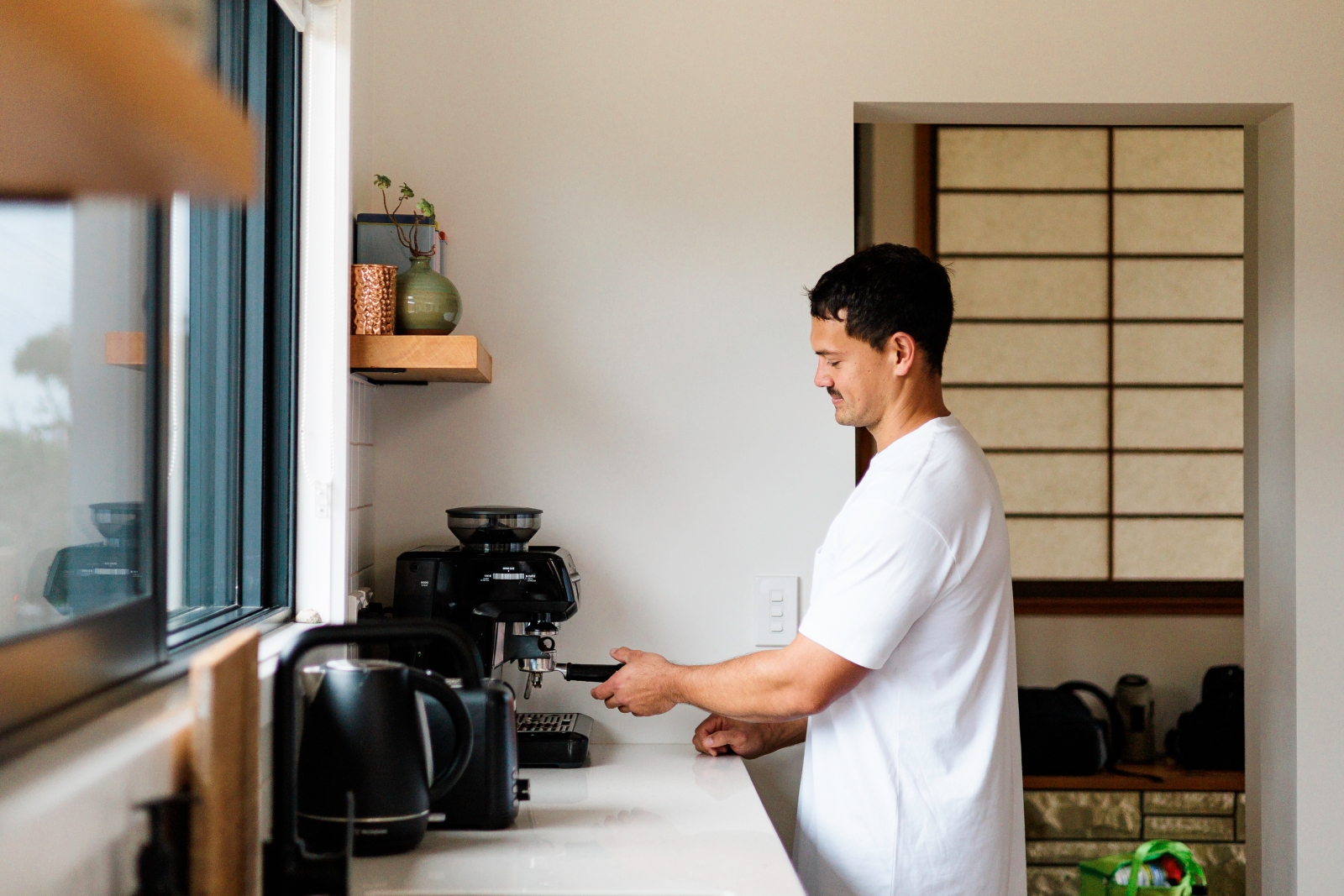 A young Māori man using a home espresso machine in the kitchen.