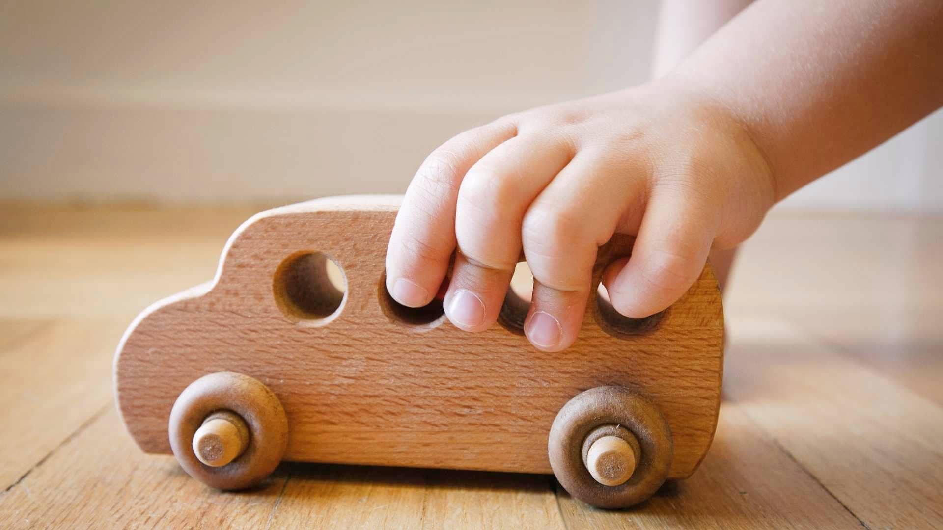 Toddler playing with a secondhand wooden car toy on the floor of the living room.