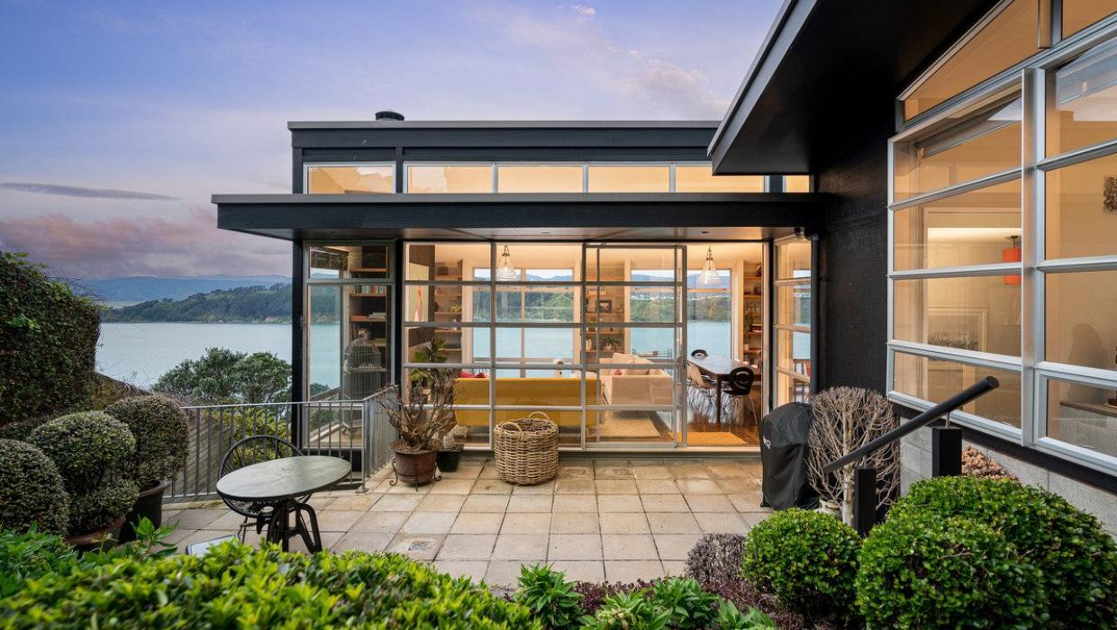 At the top of this four-and-a-half-level home in Roseneath, Wellington, the main living area opens out to a landscaped patio. The lines of the windows and stacker doors reflect a distinct Modernist influence. Photo: Lowe & Co