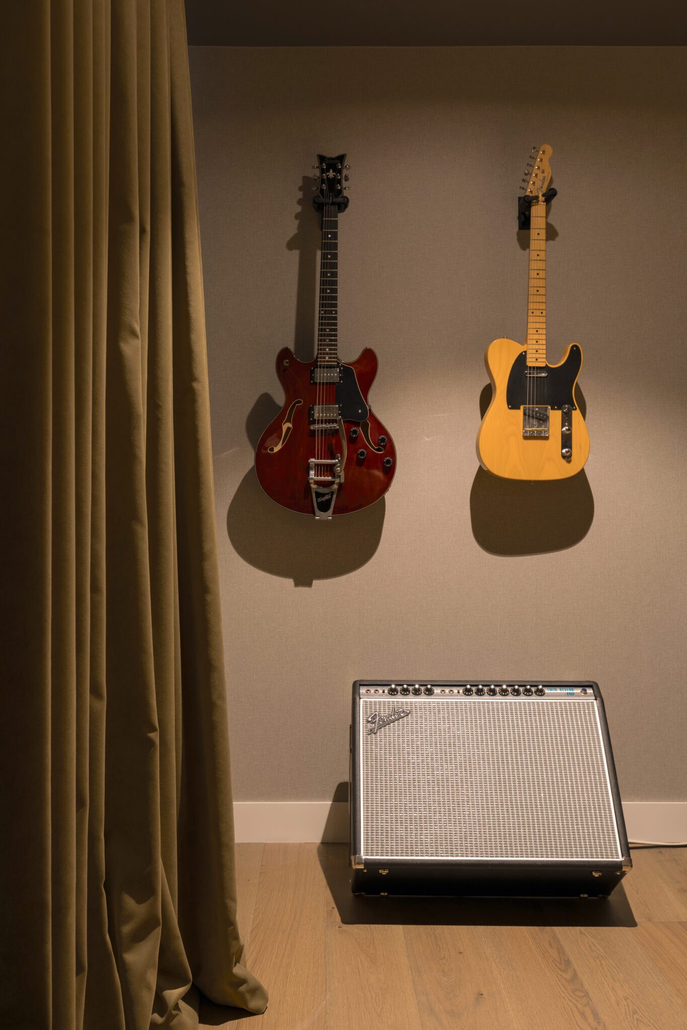 Acoustic room with beige curtains, two guitars mounted on the wall, and a Fender amplifier on a wooden floor.