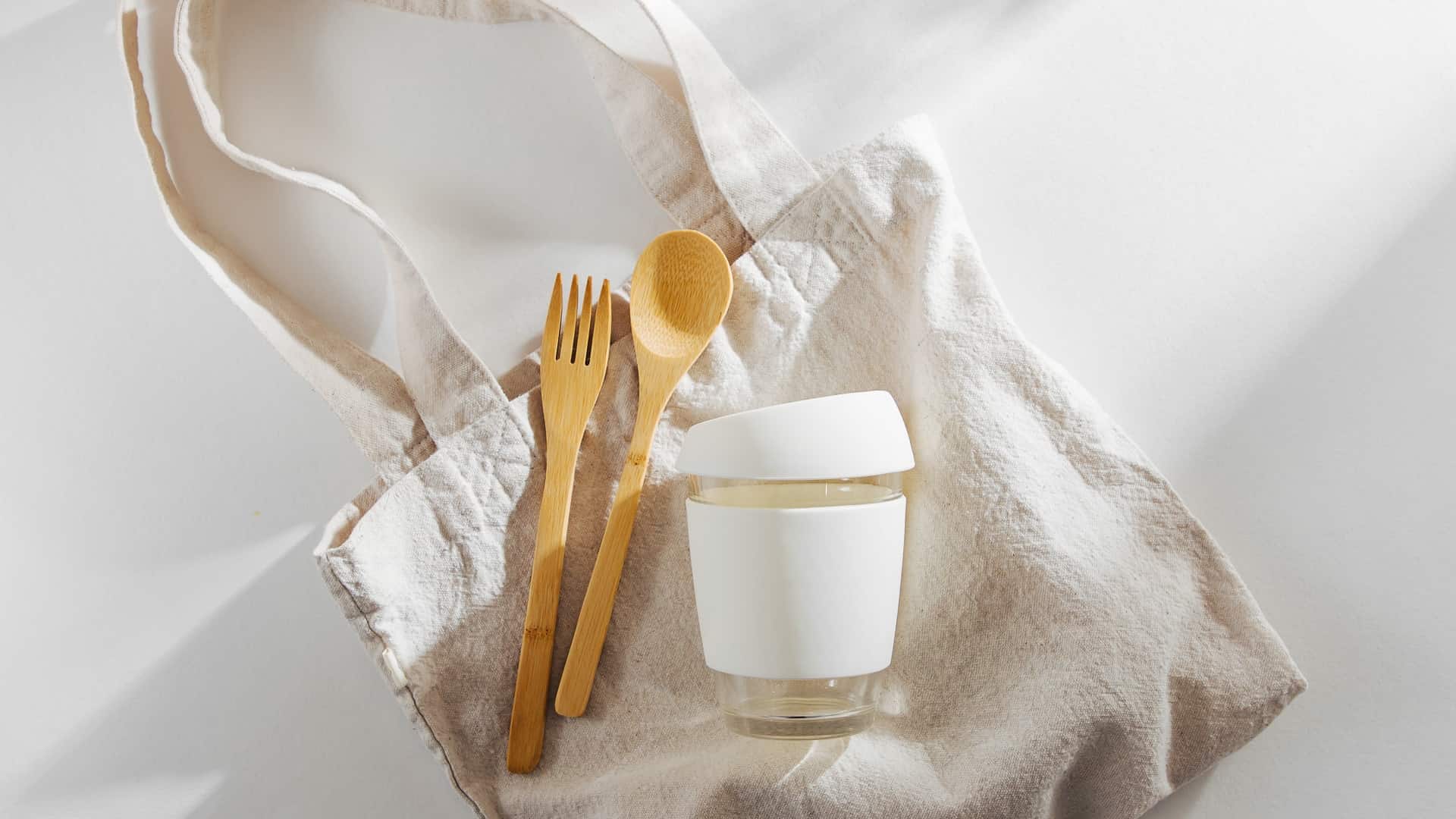 A canvas tote with a keep cup and bamboo cutlery.