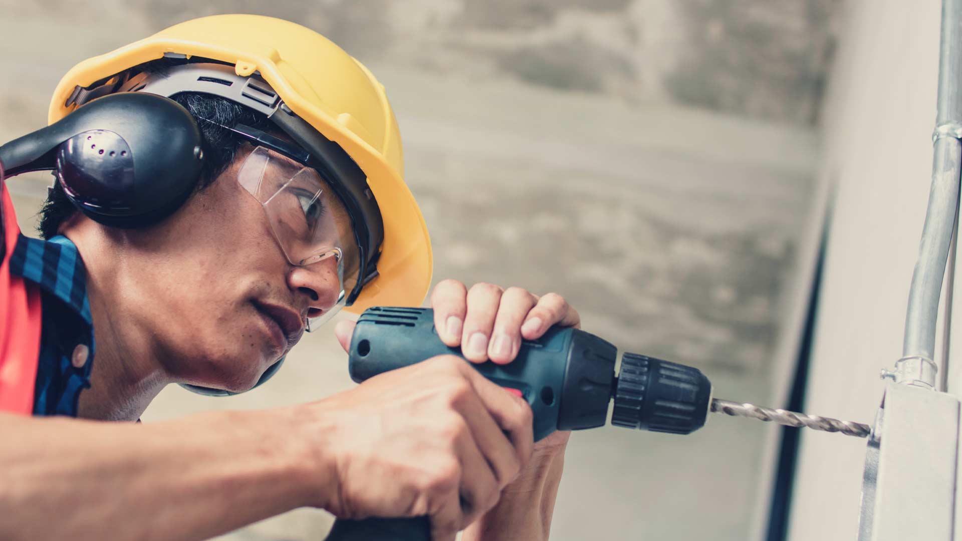 Employee using a drill with a hard hat on.