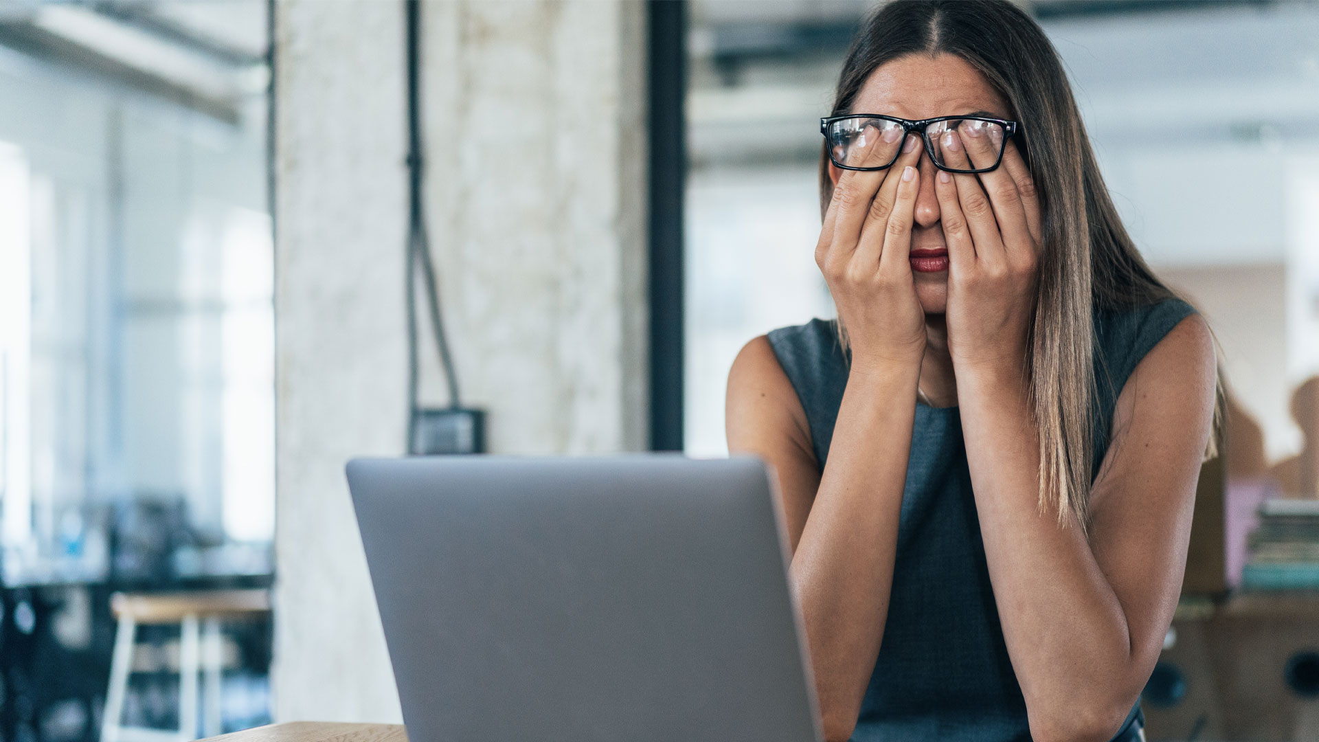 Stressed out manager sitting at her laptop in an office with her head in her hands.