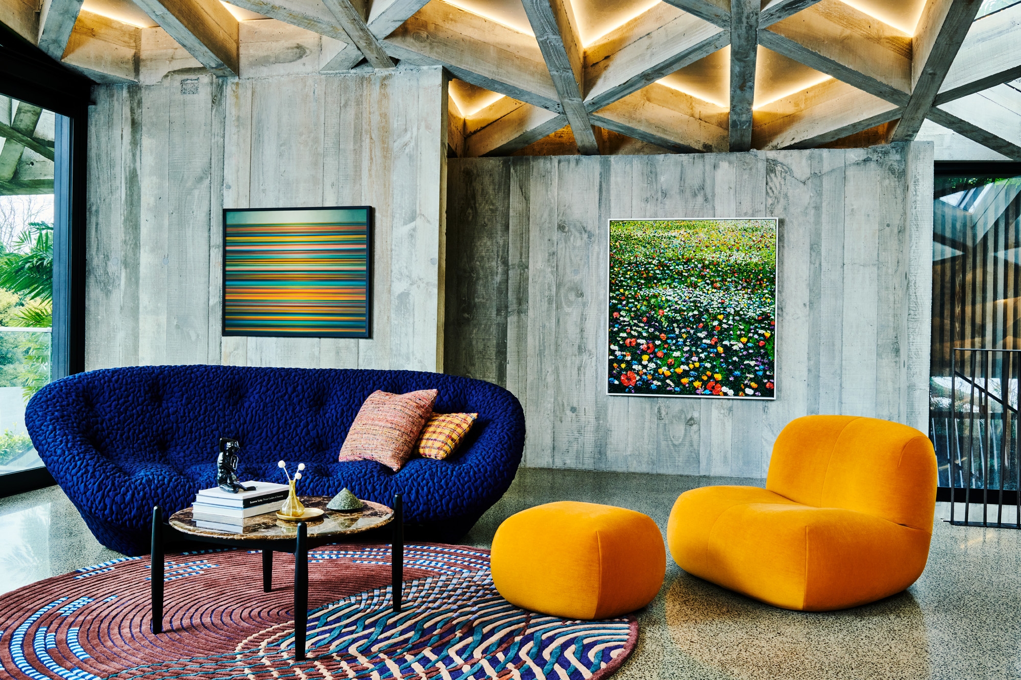 Bright blue sofa and orange armchair sit on a circular carpet with paintings hanging in the background