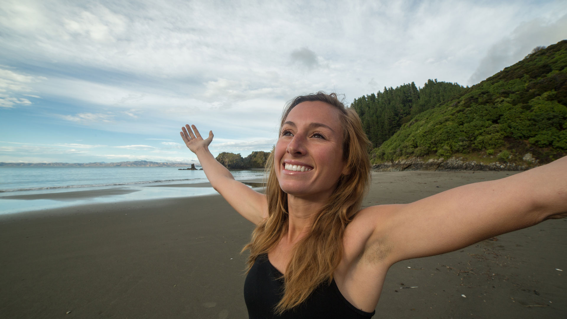 A very happy woman with her arms up in the air on a Marlborough beach.