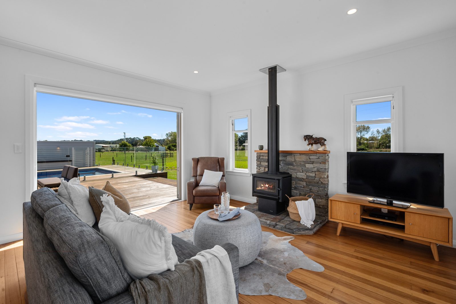 Lounge with TV, fireplace and sofa with open doors overlooking pool and paddocks.
