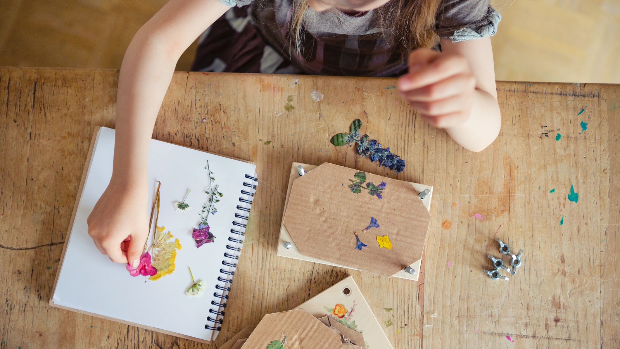 Young girl creating a scrapbook using flower cuttings at a wooden table at home.