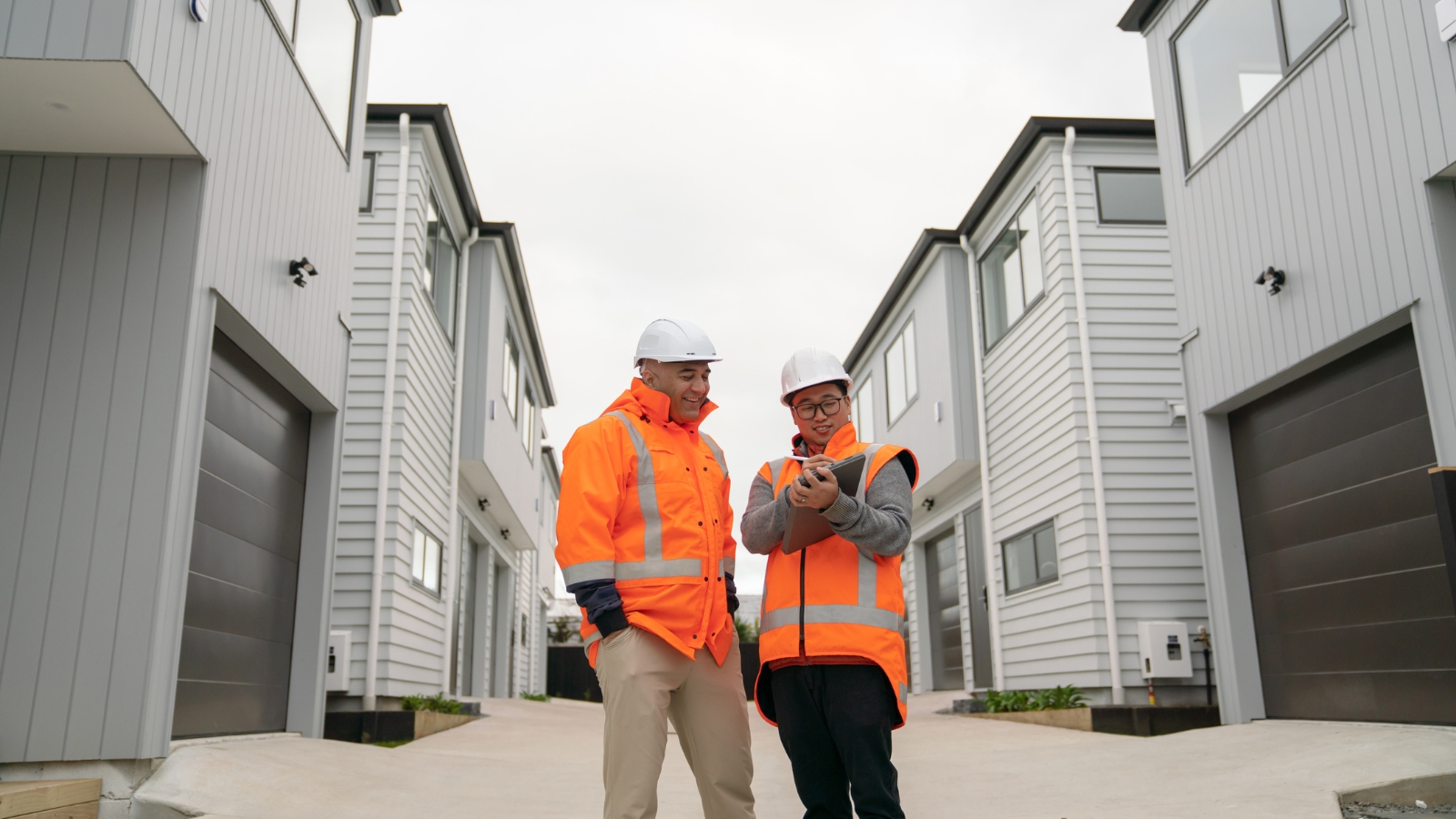 Two men in high vis jackets looking at townhouses. 