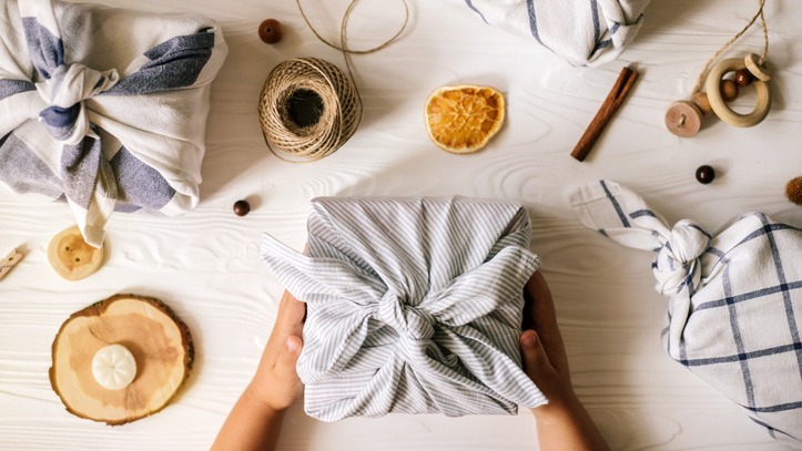 3 gifts wrapped in tea towels, surrounded by twine, dried fruit and wooden beads.