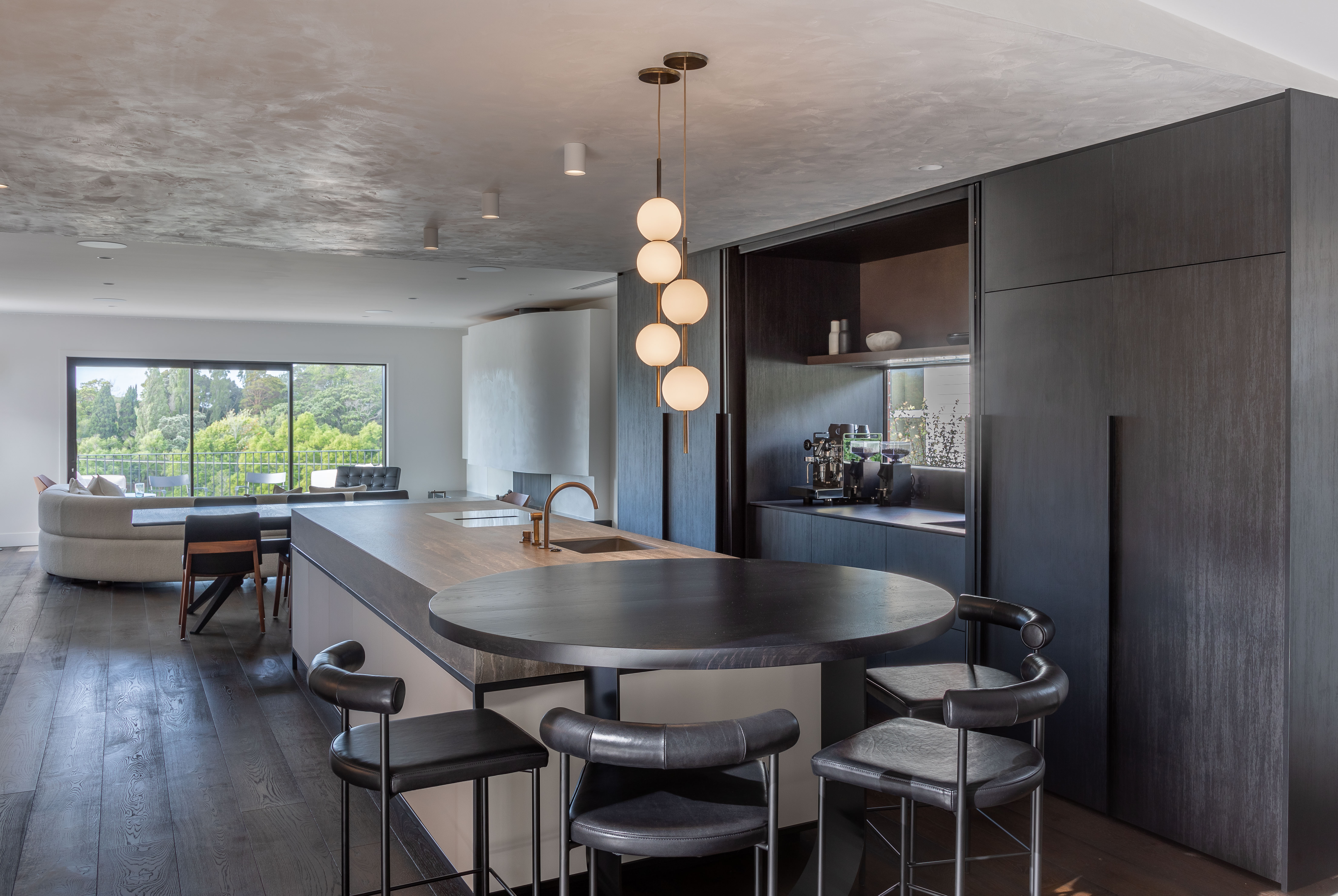 This open-plan kitchen and living area designed by Katie Scott of Sticks + Stones Design cleverly incorporates downlights and sculptural pendants to enhance the textures and beauty of the materials. Image: John Williams