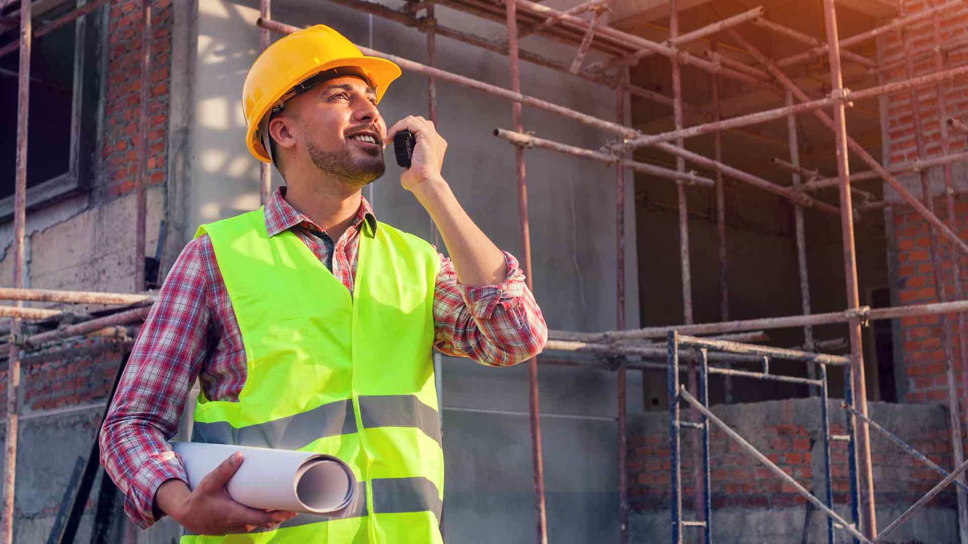 A man in a working on a construction site with a helment and high-vis jacket.