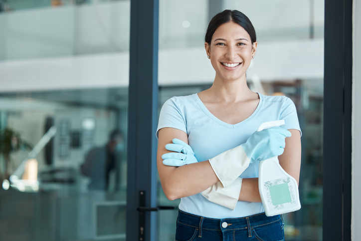 Woman standing with arms crossed holding cleaning products 