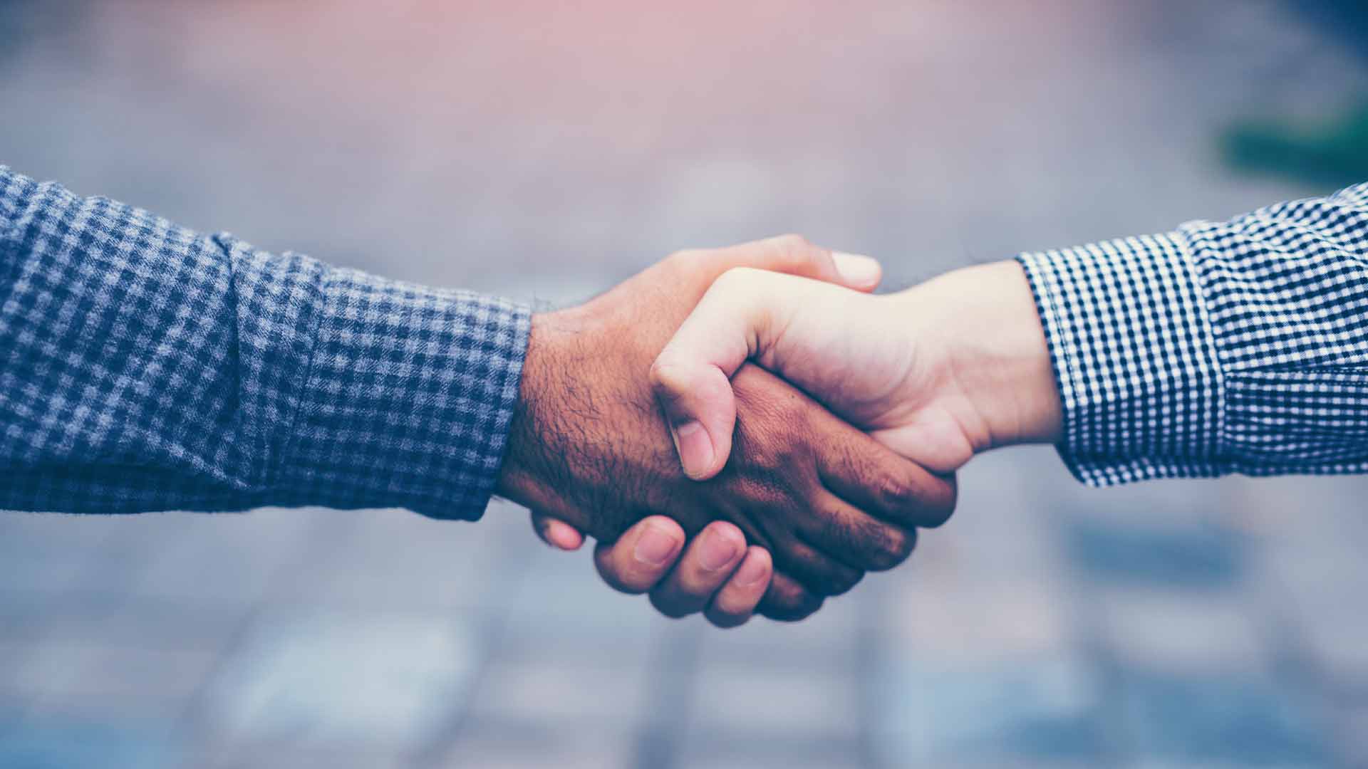 A close-up photo of two people shaking hands outside.