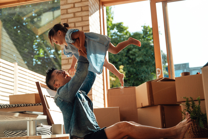A person sitting with his child and a stack of moving boxes, capturing the transition between selling and buying a home.