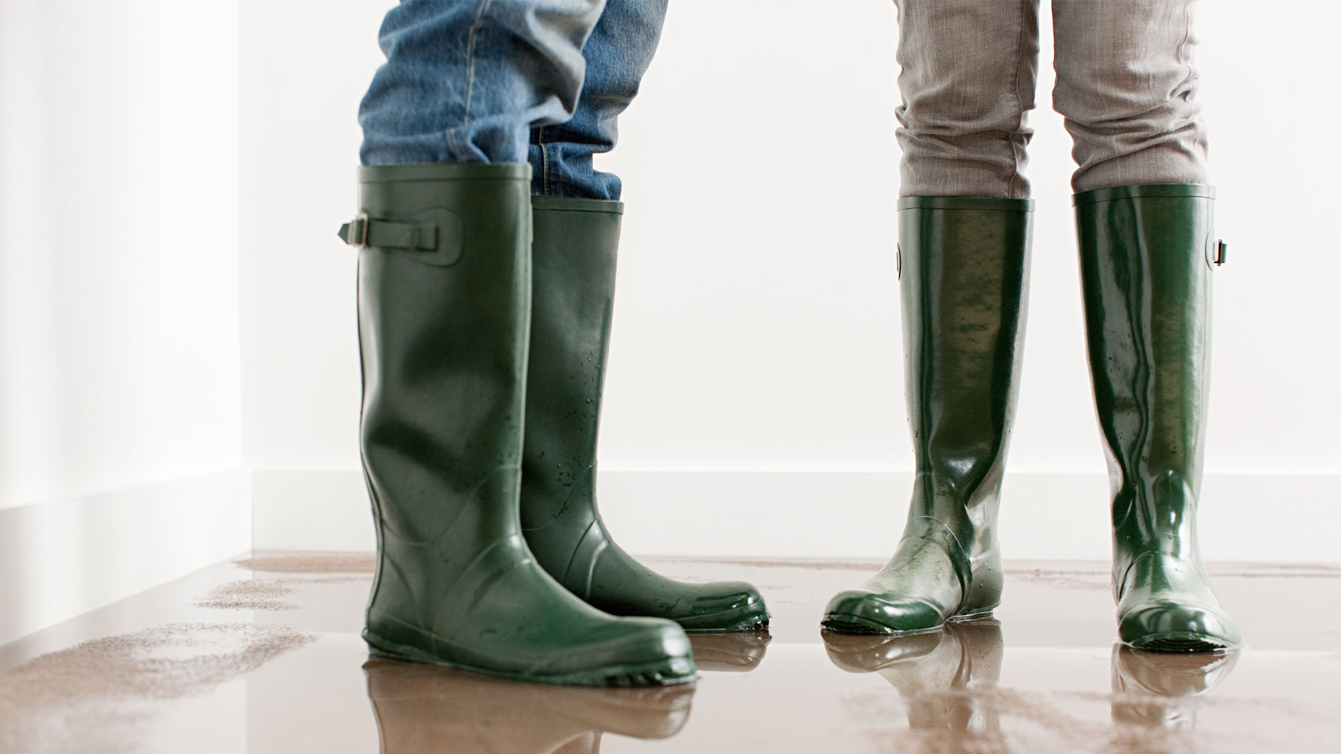 People standing in gum boots inside a flooded home following a natural disaster.