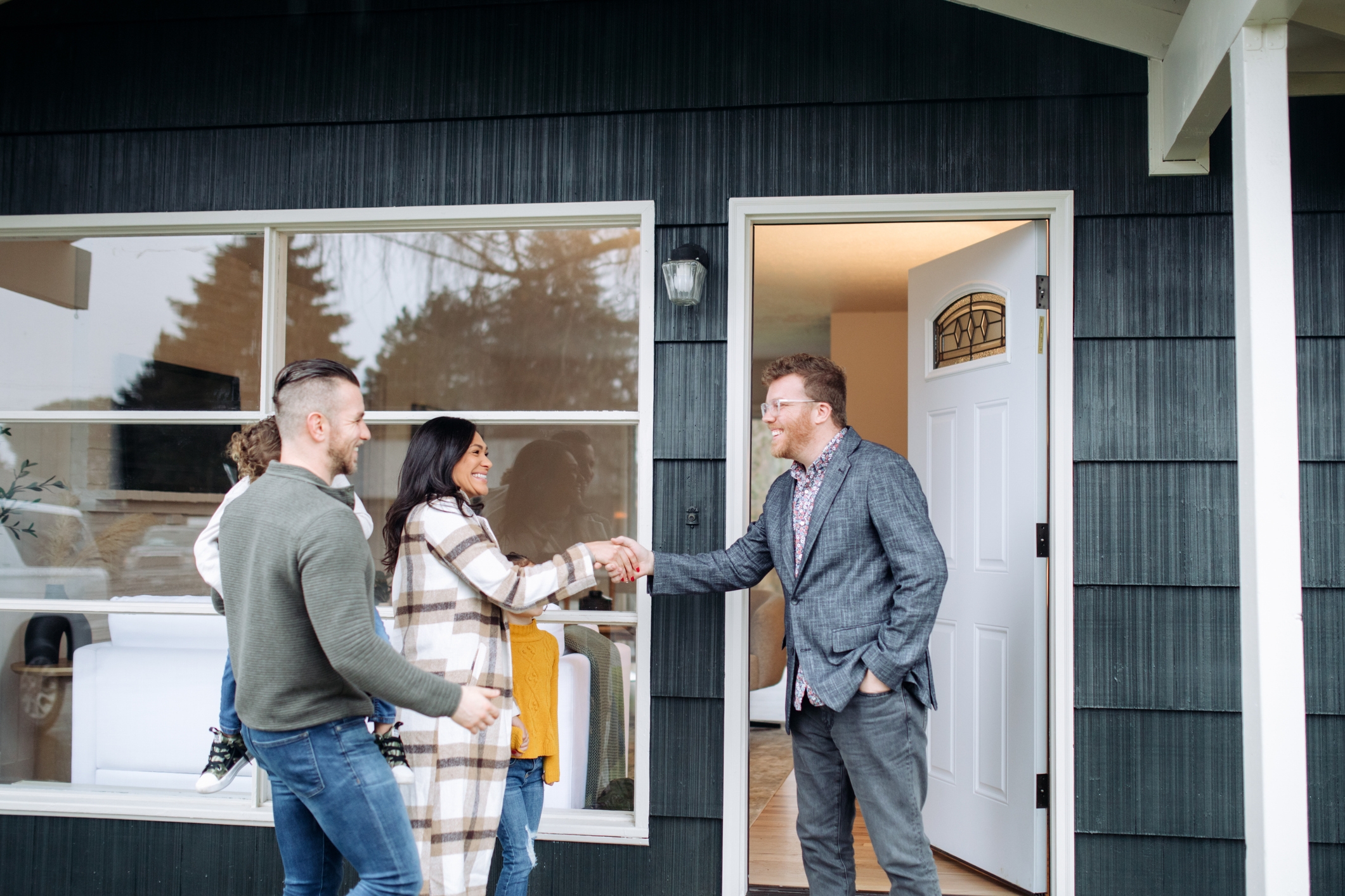 Woman and man buyers shaking hands with a real estate agent in front of a house