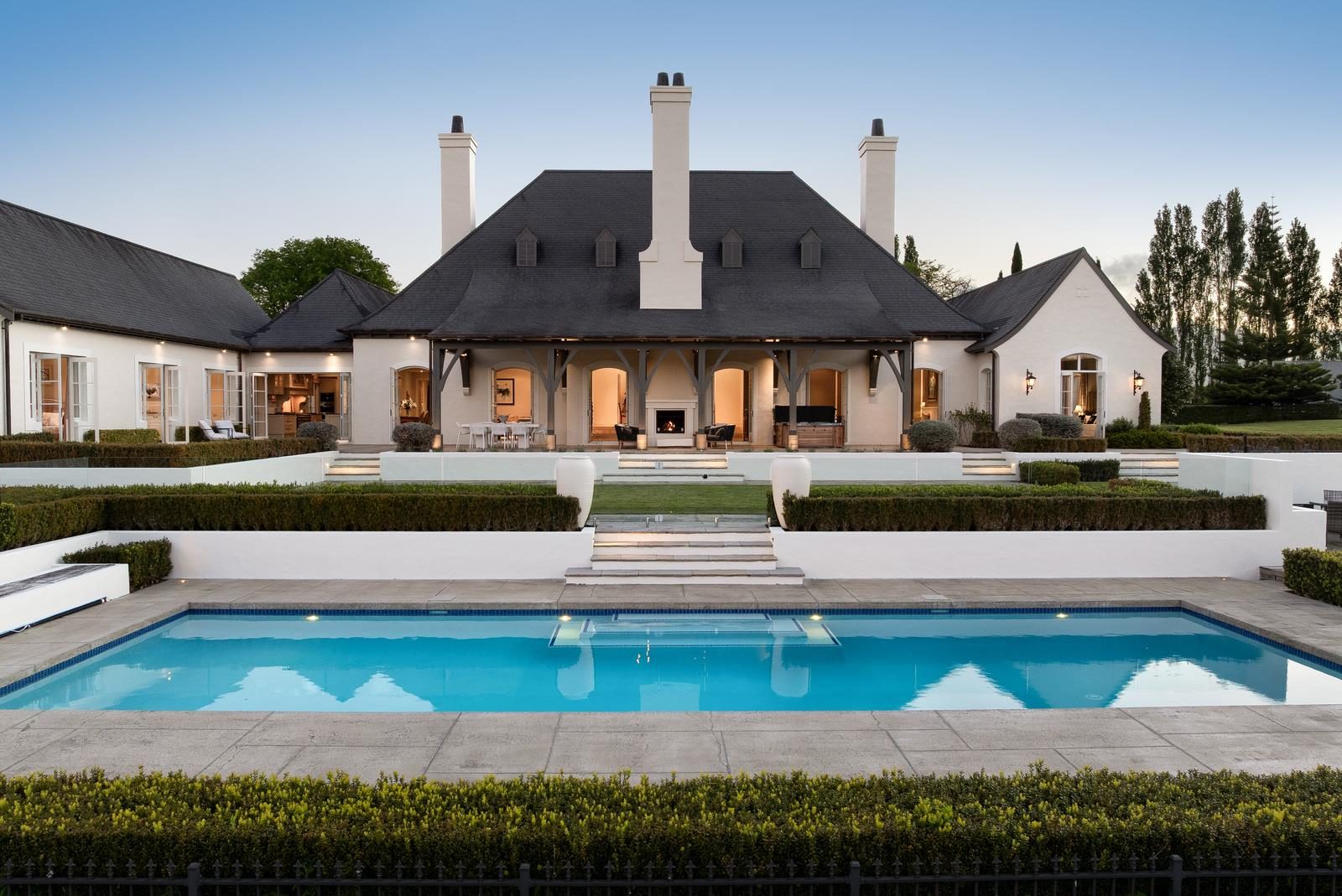 White estate home with outdoor fireplace, pool, manicured hedging and multiple chimneys at 4 Lewis Lane, Coatesville, Auckland