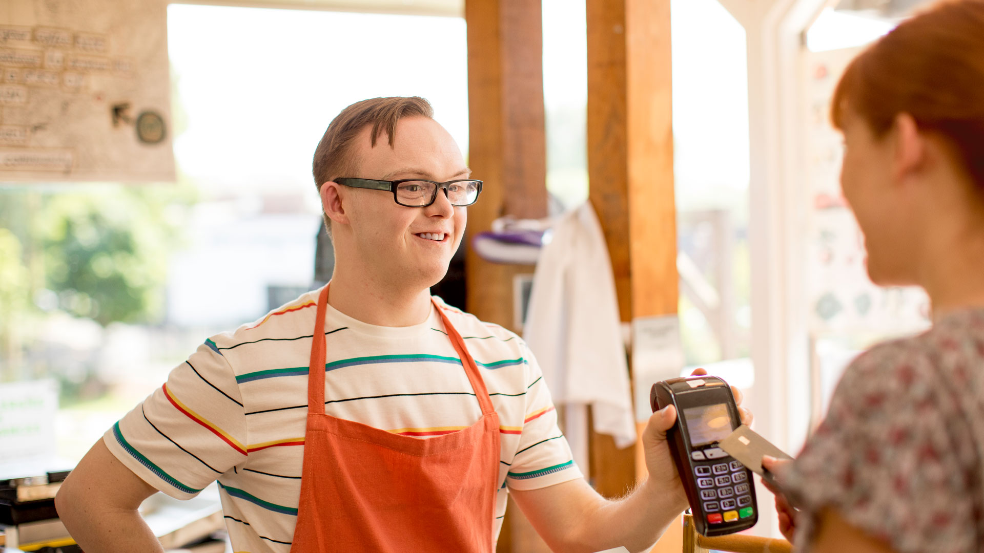 Young man working in a retail outlet handing a customer an eftpos machine to pay for their goods.