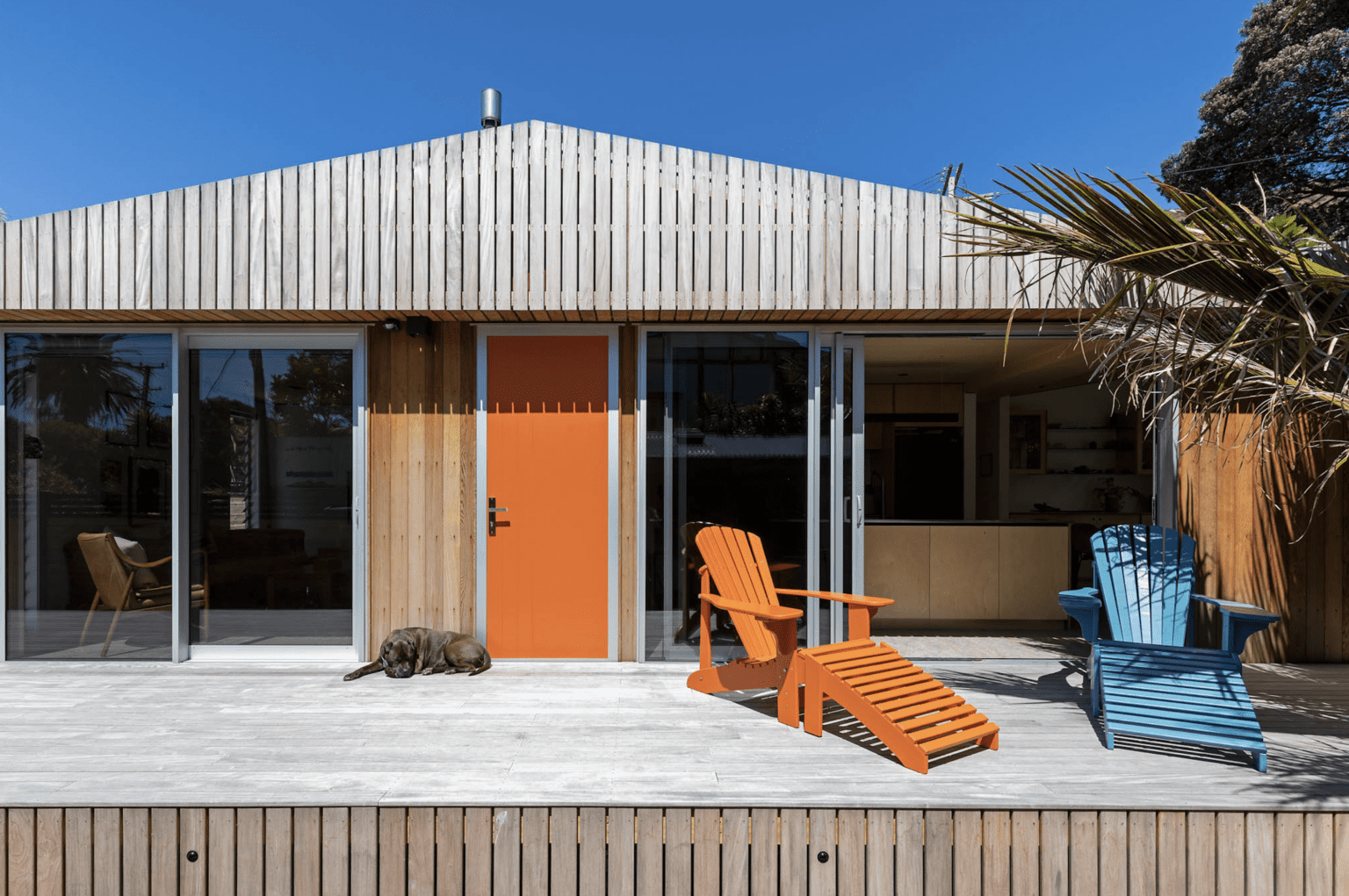 Bright orange and blue deck chairs on brown wooden deck. Orange front door.