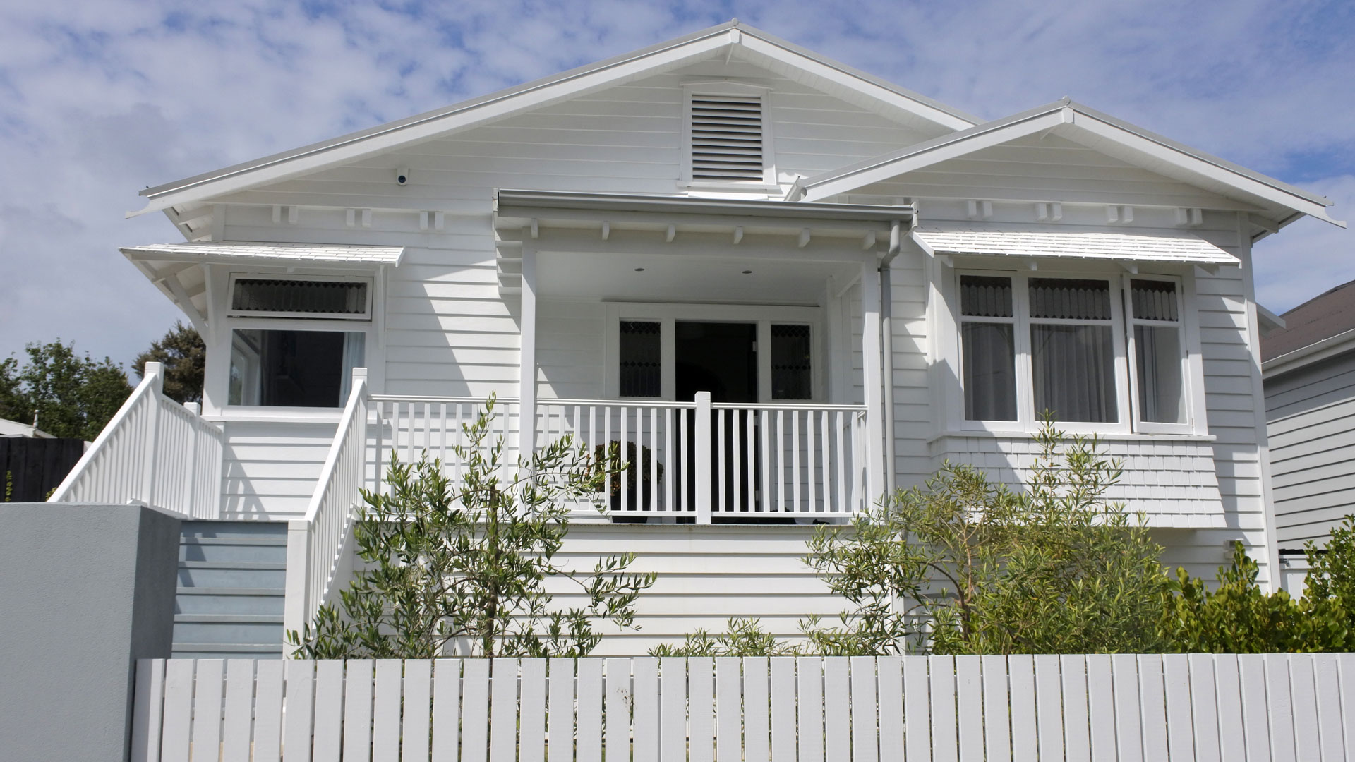 White wooden Auckland property for sale with the sun on it.
