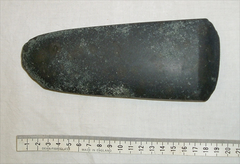 greenstone toki axe head next to a measuring tape 