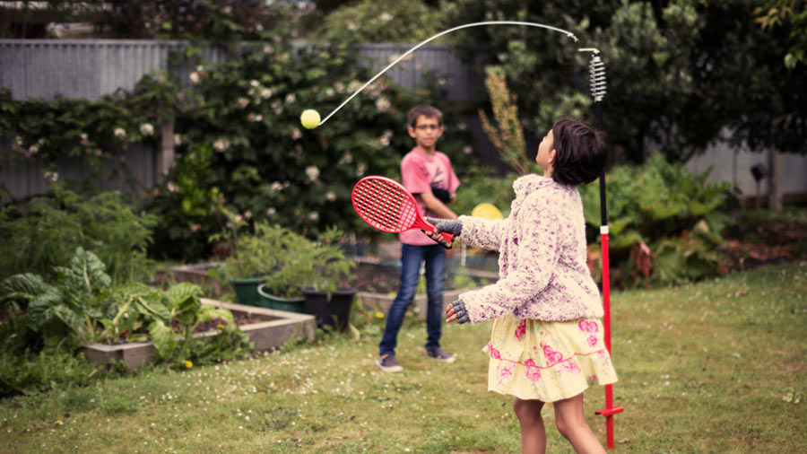 A brother and sister playing swingball in the back garden of their home.