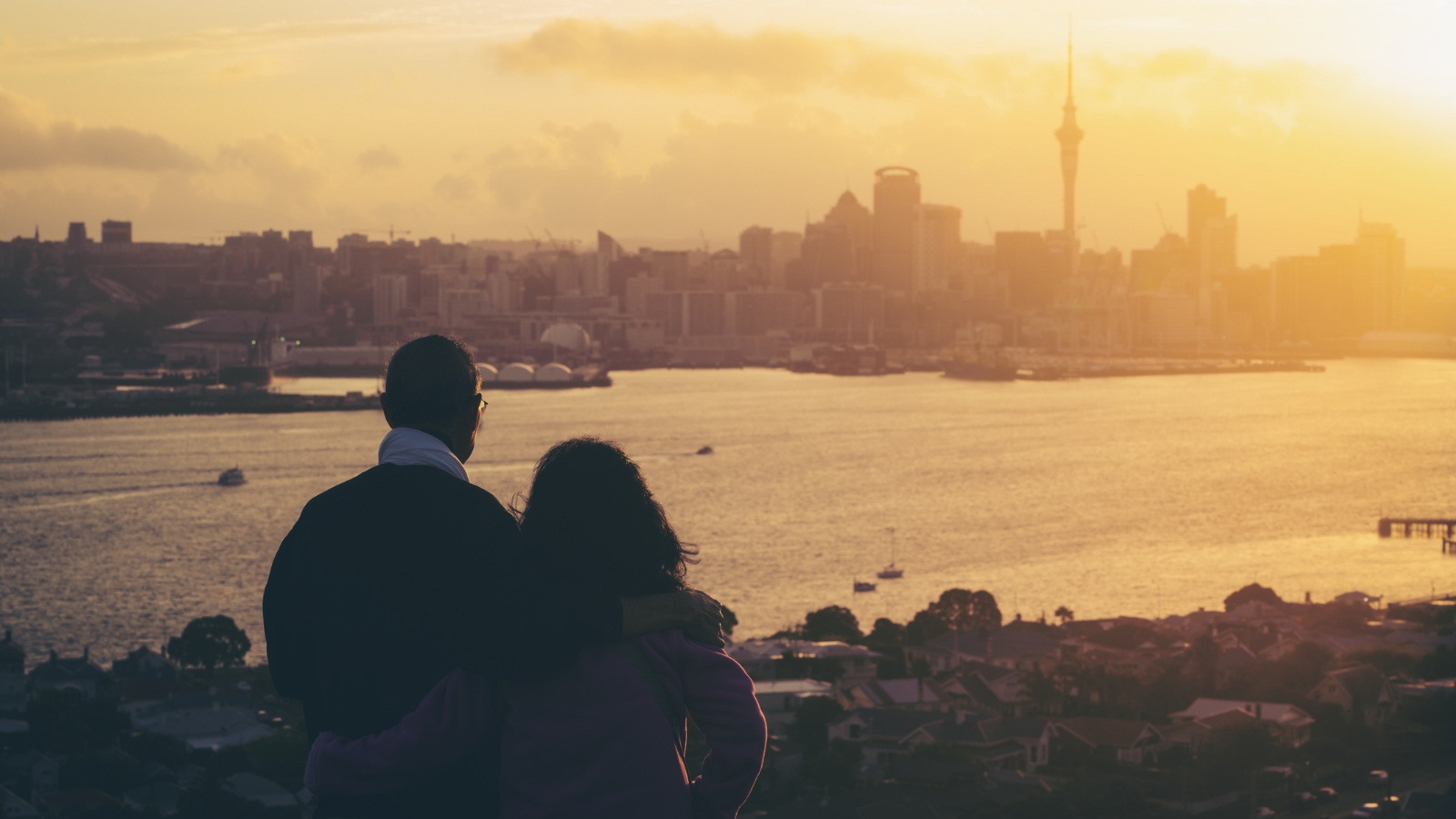 Couple looking out across harbour over Auckland city. 