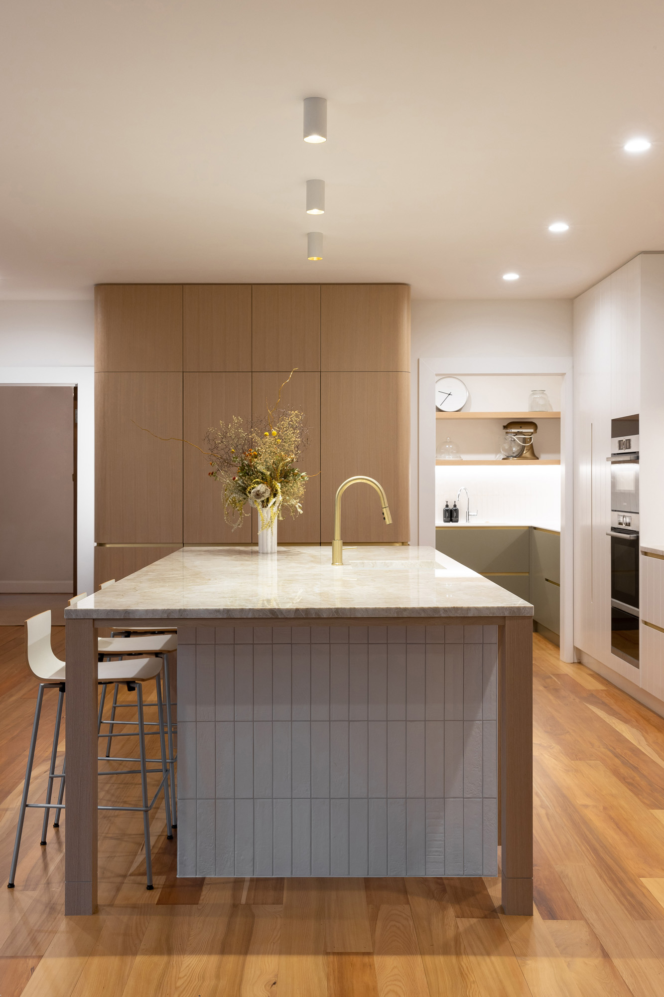 Pantry with timber shelves matching the kitchen's timber cabinetry, with a unified color palette connecting both spaces.