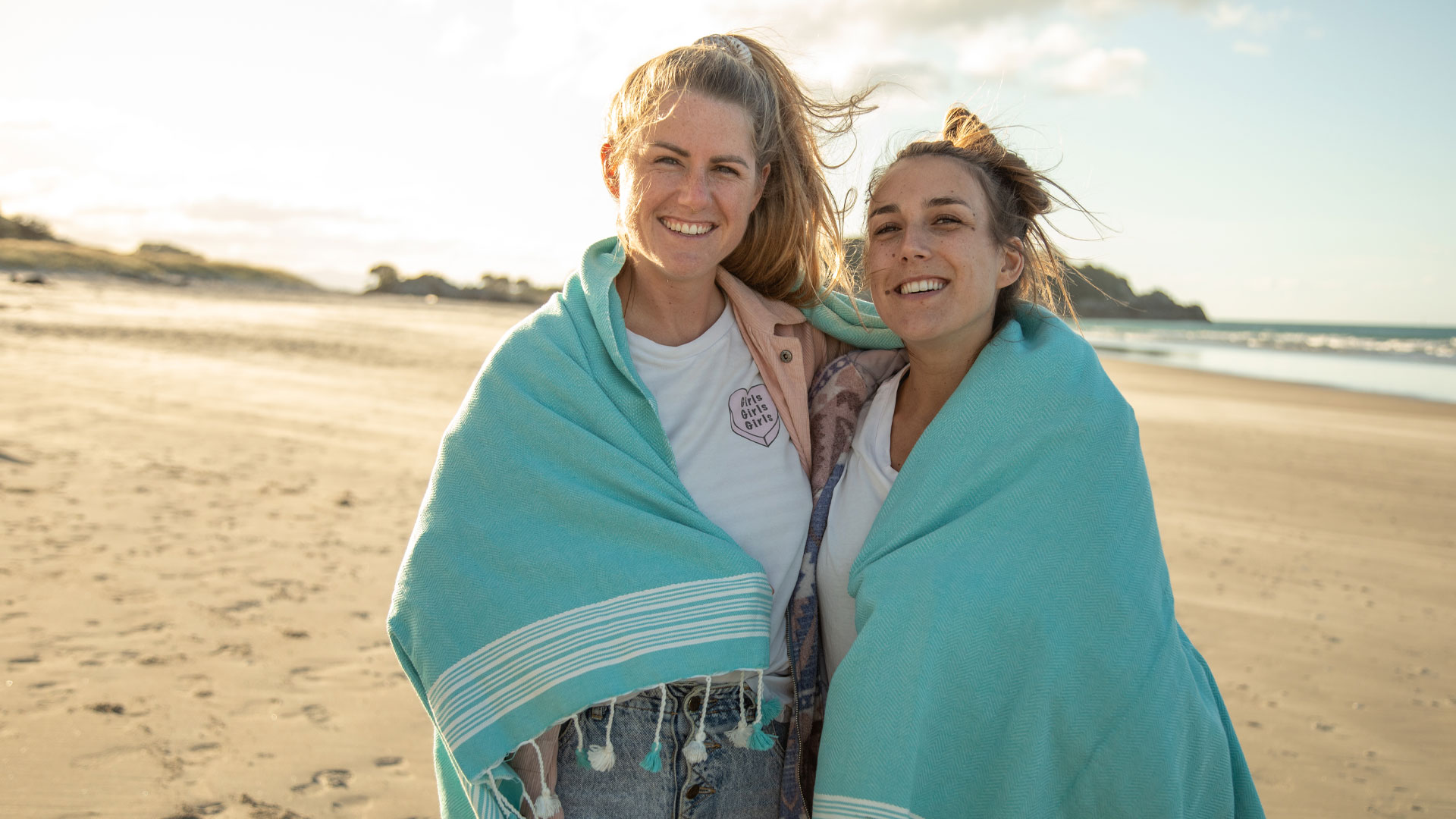 Lesbian couple on a beach in the Bay of Plenty with a blue shawl over their shoulders.