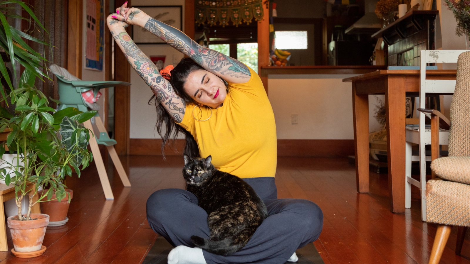 Woman in yellow shirt doing yoga with cat on her lap. 