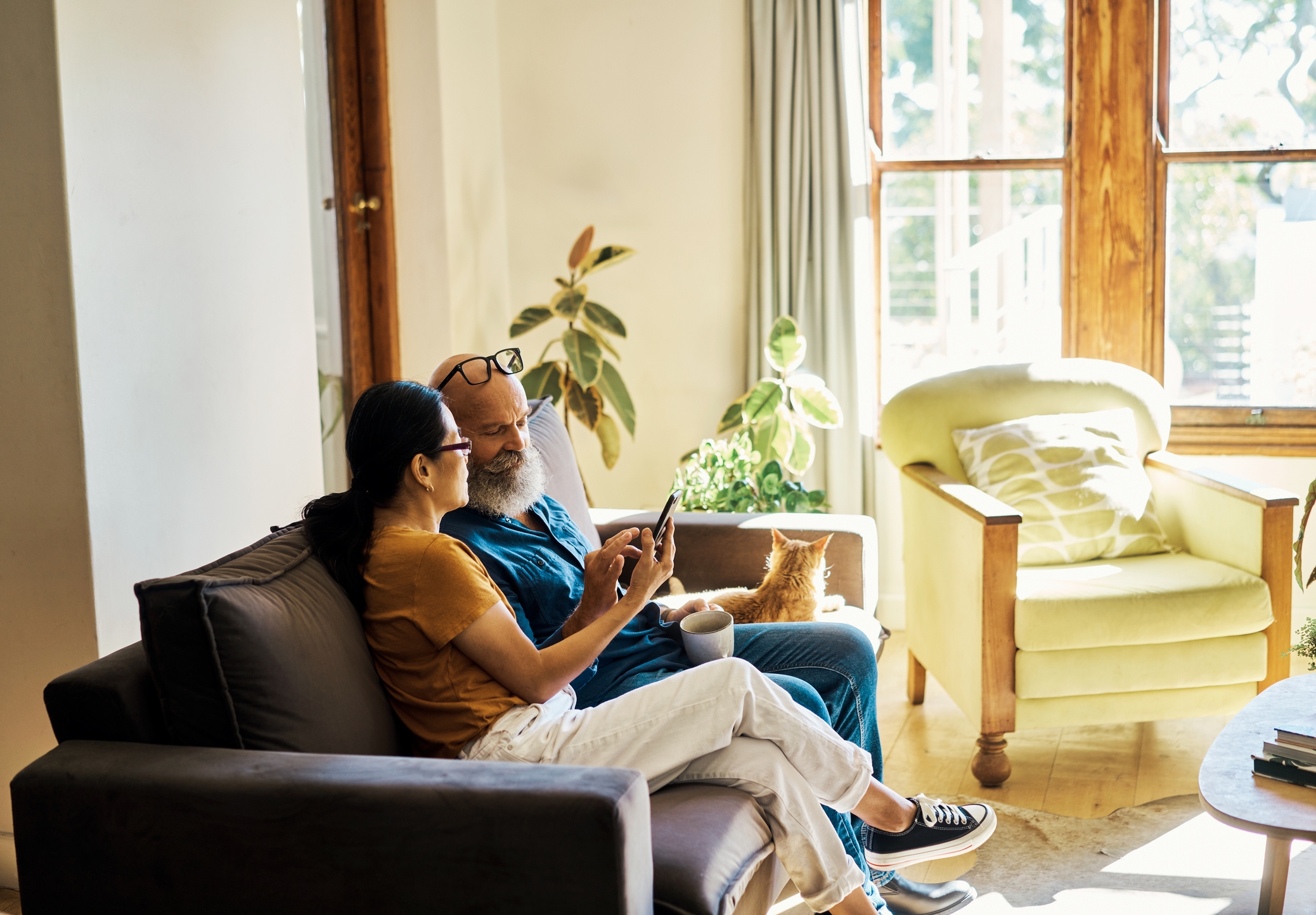 Woman and man sit on a couch as she helps him search on his mobile phone.