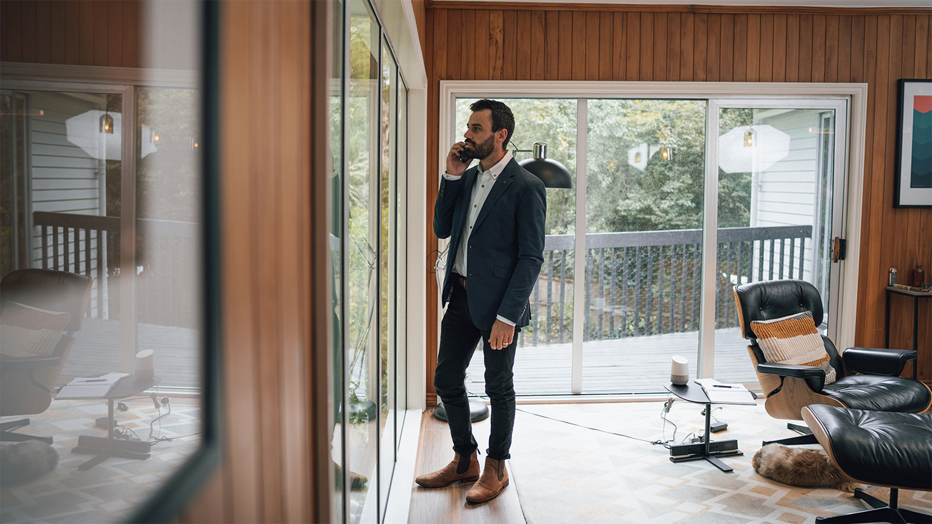 Man in a suit at home looking out of the window while talking on his cell phone.