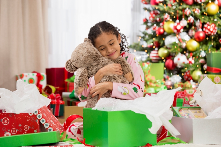 Little girl opens Christmas present and hugs a teddy bear