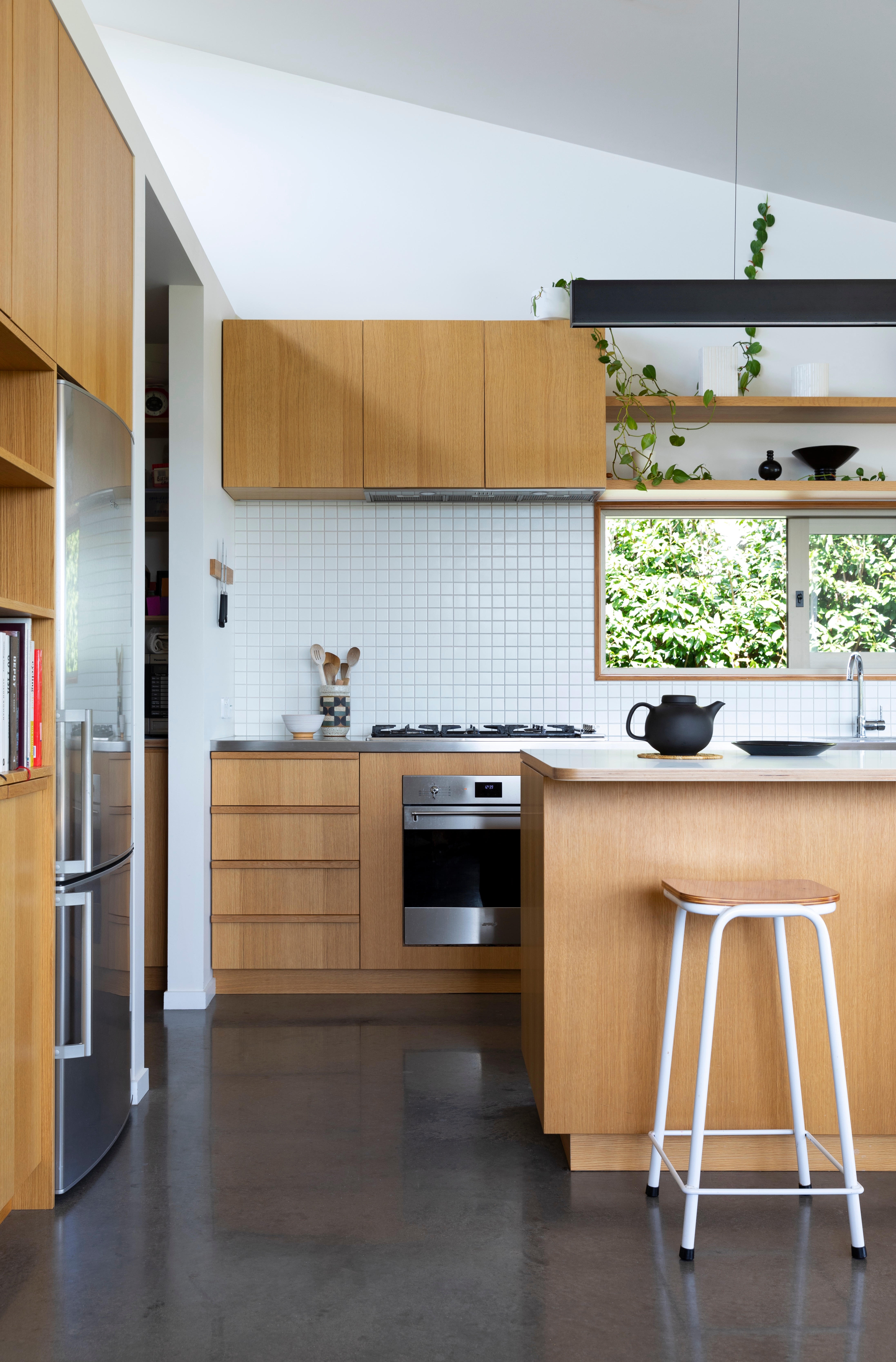 In the kitchen, the American oak cabinets meet a stainless steel bench. Some of the décor details here include a light by Linetec over the island, an Olio teapot by Barber Osgerby x Royal Doulton and stools from Flotsam & Jetsam.