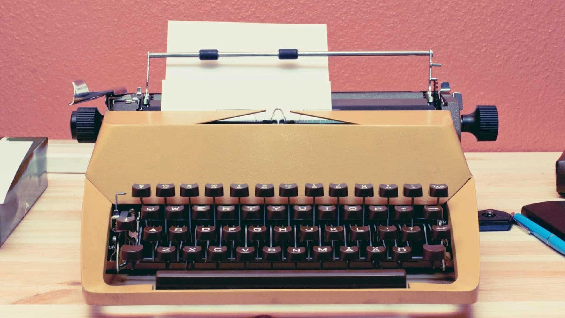 Yellow typewriter with black keys on a wooden desk with a red wall behind it