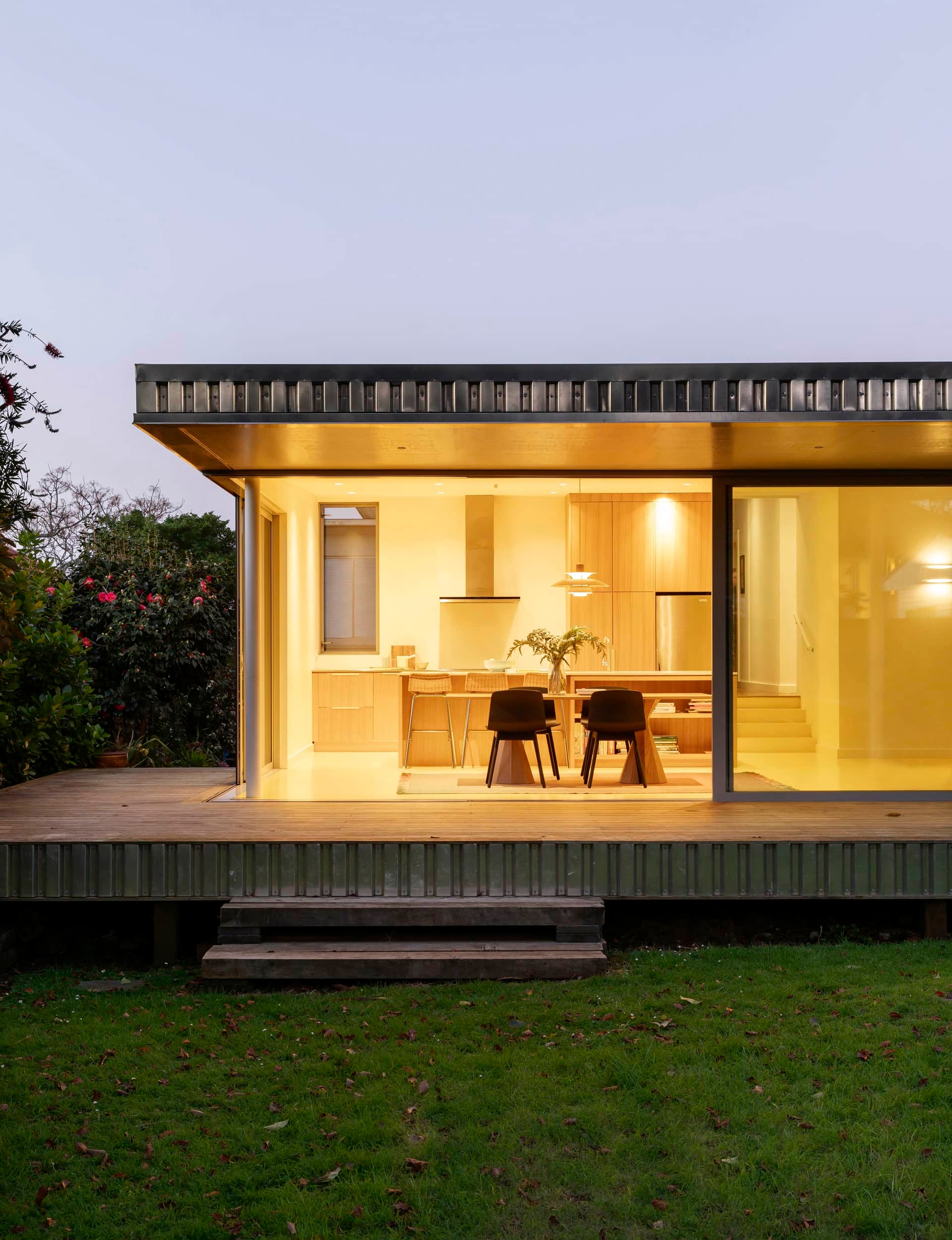 View from outside of a small, open-plan modern kitchen with the lights on at night