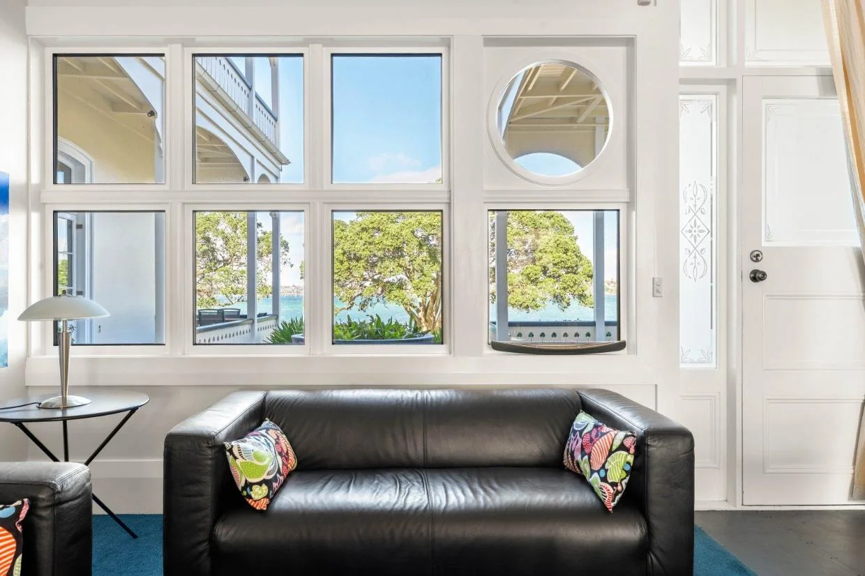 The view is framed by pōhutukawa - the porthole window is one of three on the front of the building.