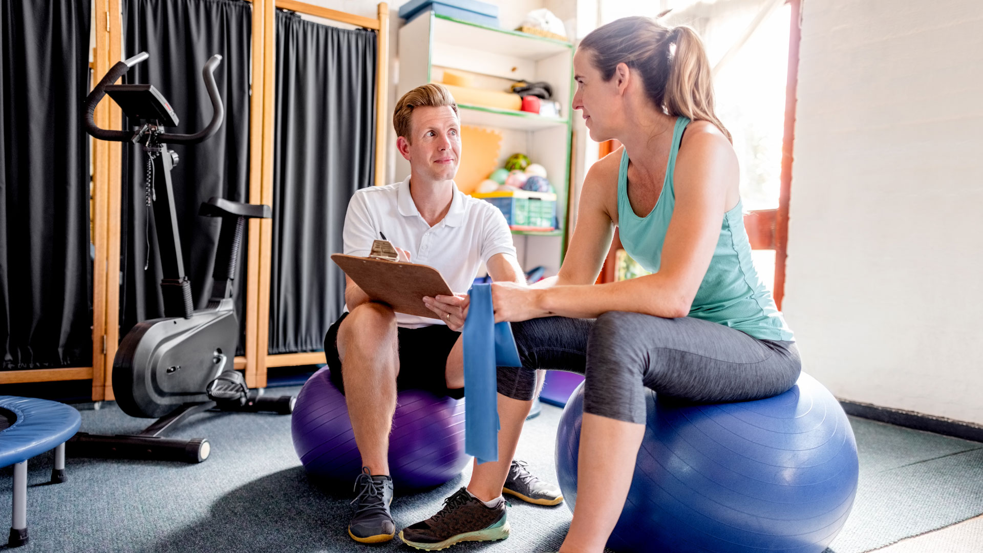 Physiotherapist sitting on a swiss ball with a client and discussing her treatment requirements.