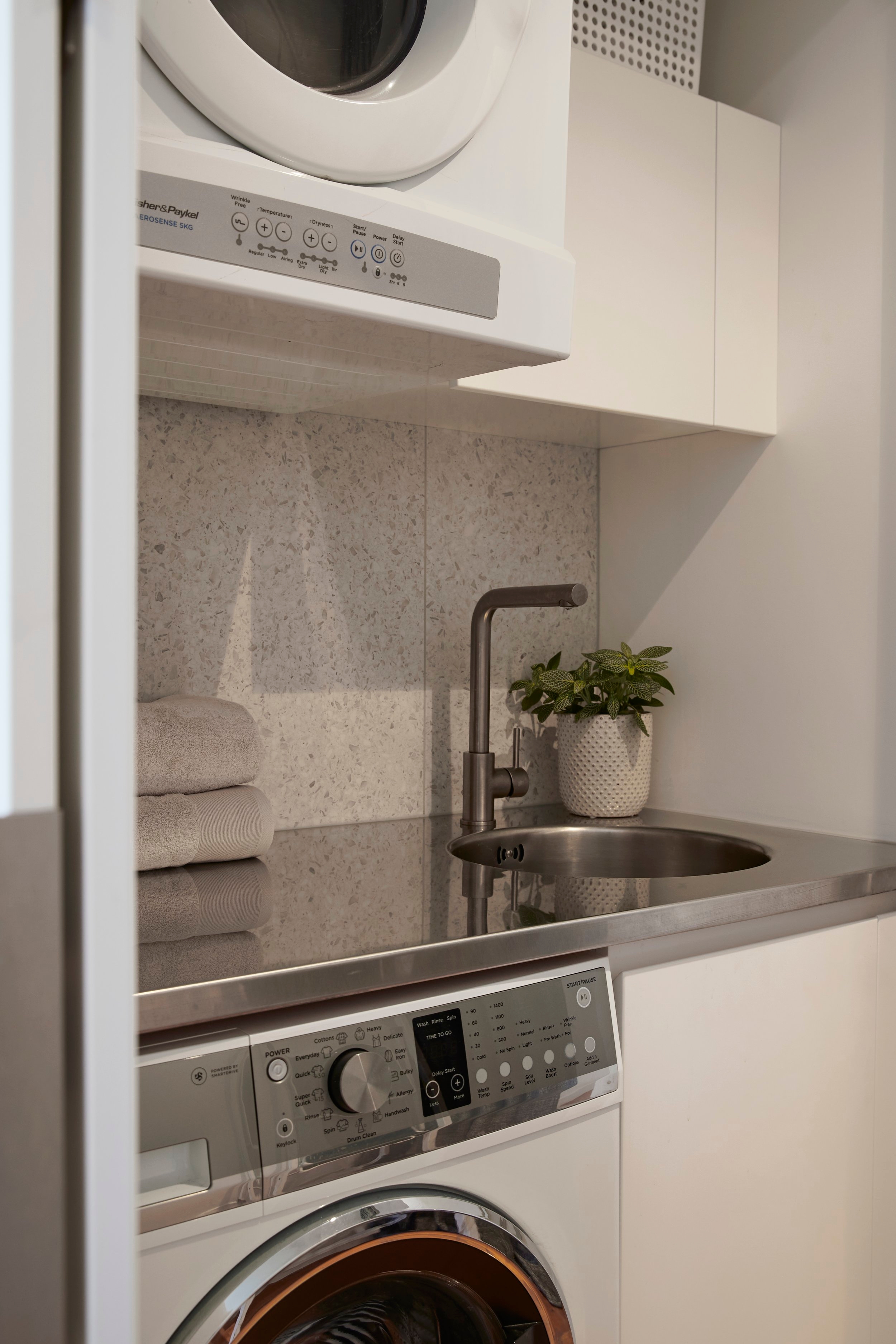 A small laundry room featuring a washing machine, dryer, and a compact metal sink, efficiently designed for limited space.