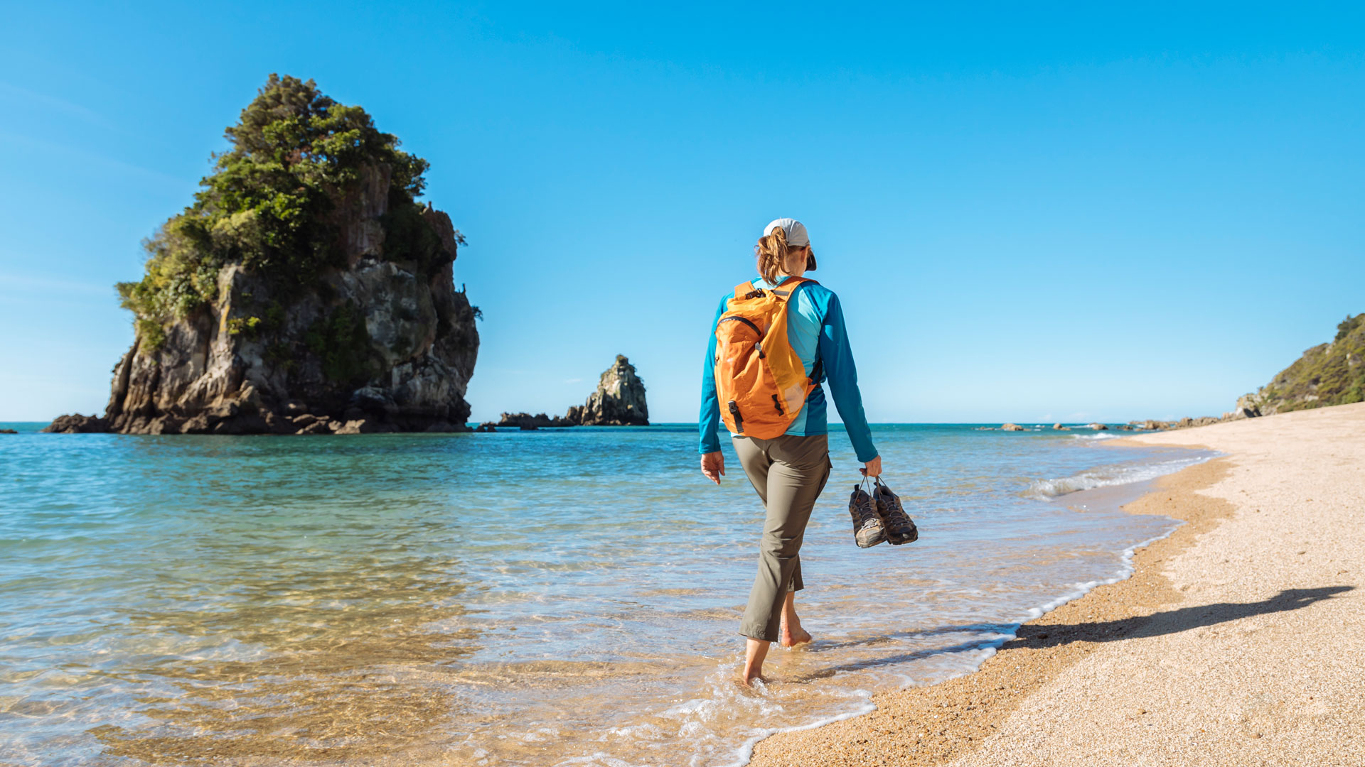 A woman walking in the shallows along a beach on a sunny day in the Nelson/Tasman region.