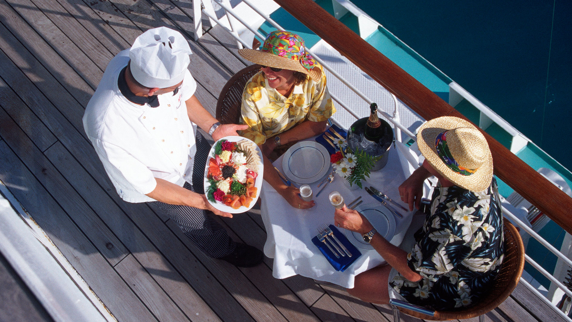 Yacht chef delivering food to customers who are eating out on the deck.