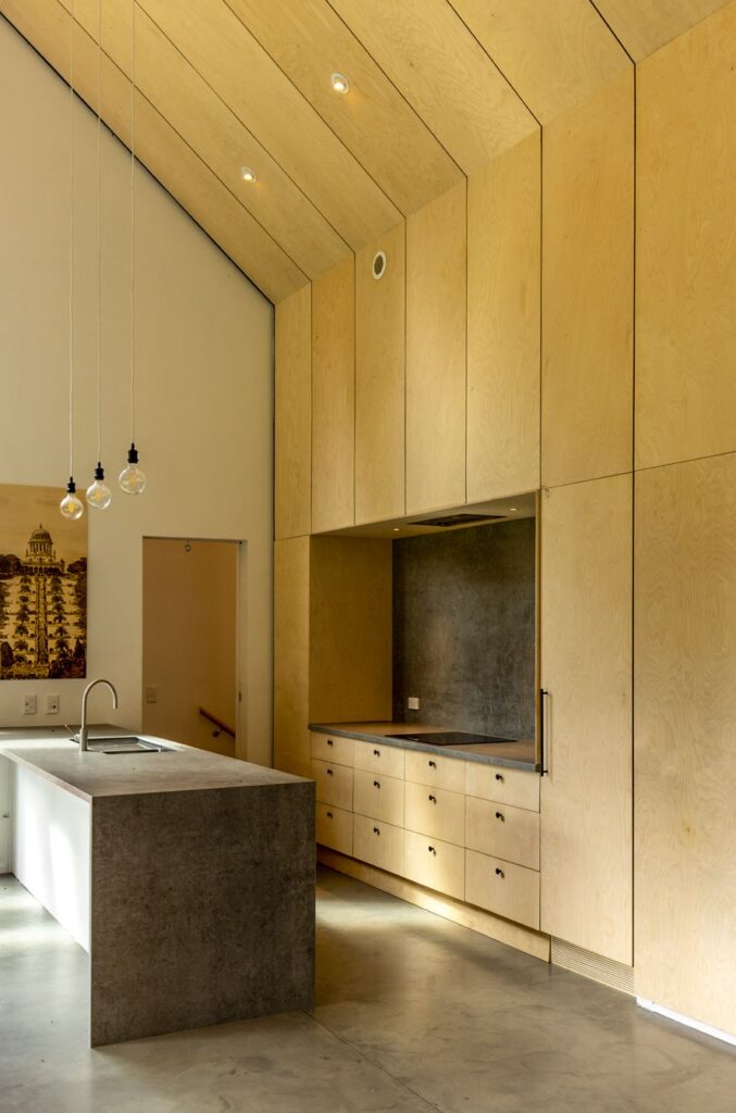 A modern kitchen with cathedral ceilings, concrete floors and a concrete bench.