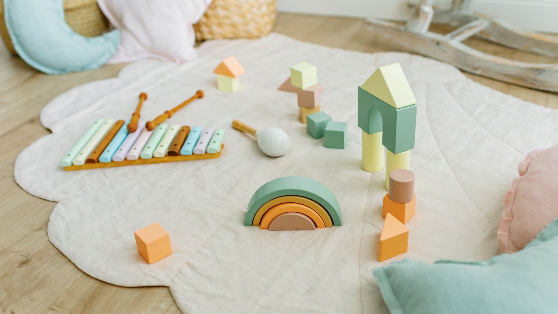 Wooden, pastel coloured children’s toys spread out on playmat in playroom.
