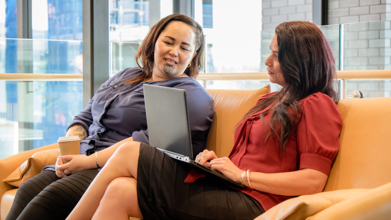 Maori woman with Moko and other woman looking at laptop.